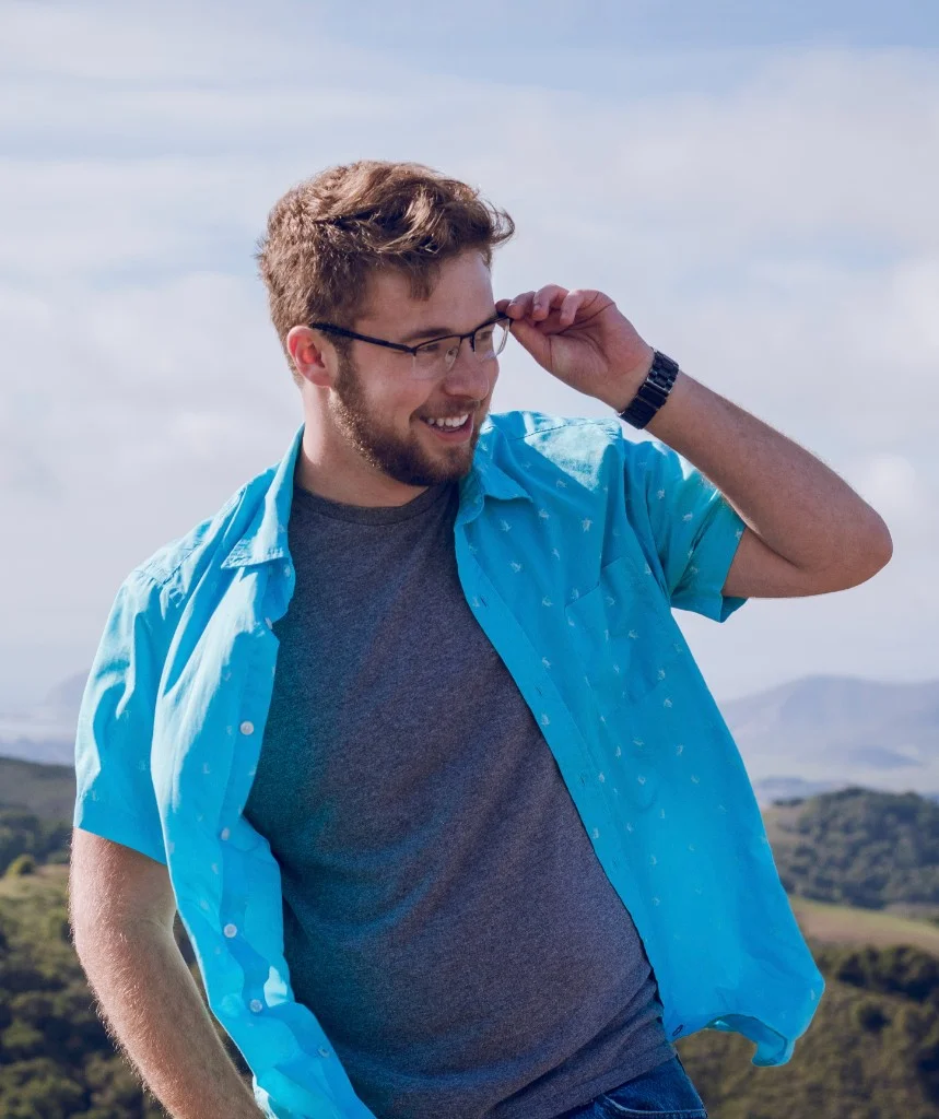 Chris Lawson outdoors in a blue patterned shirt, adjusting his glasses