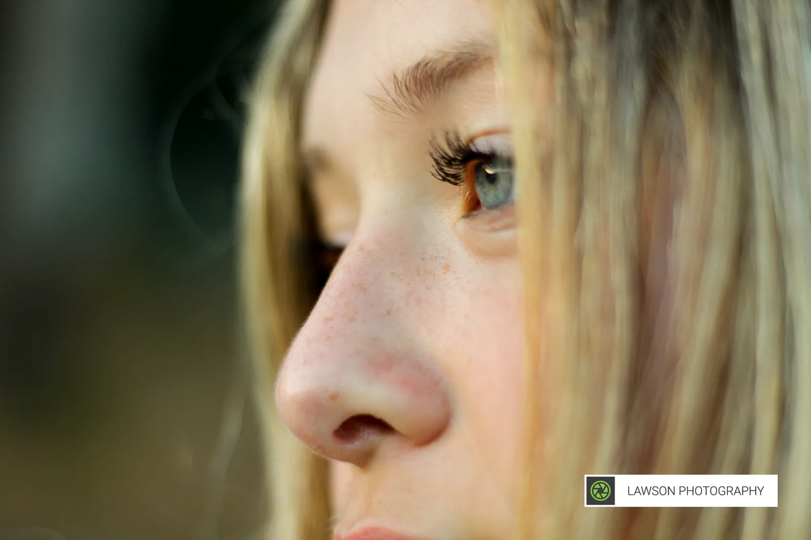 Extreme close-up profile of a young woman with blue eyes, freckles, and light hair in soft natural light.